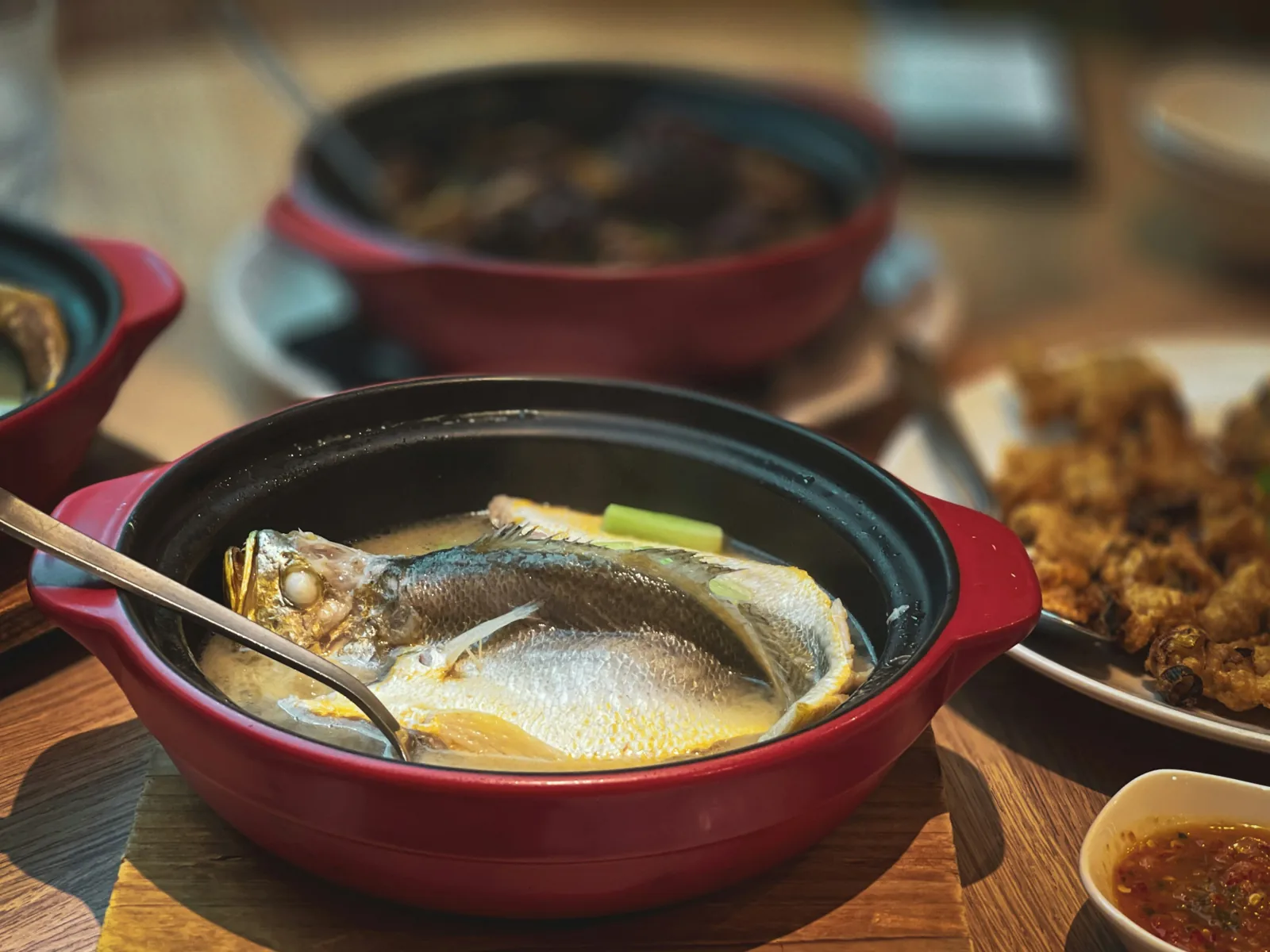 餐桌上紅色砂鍋裡燉煮的整條魚與湯勺